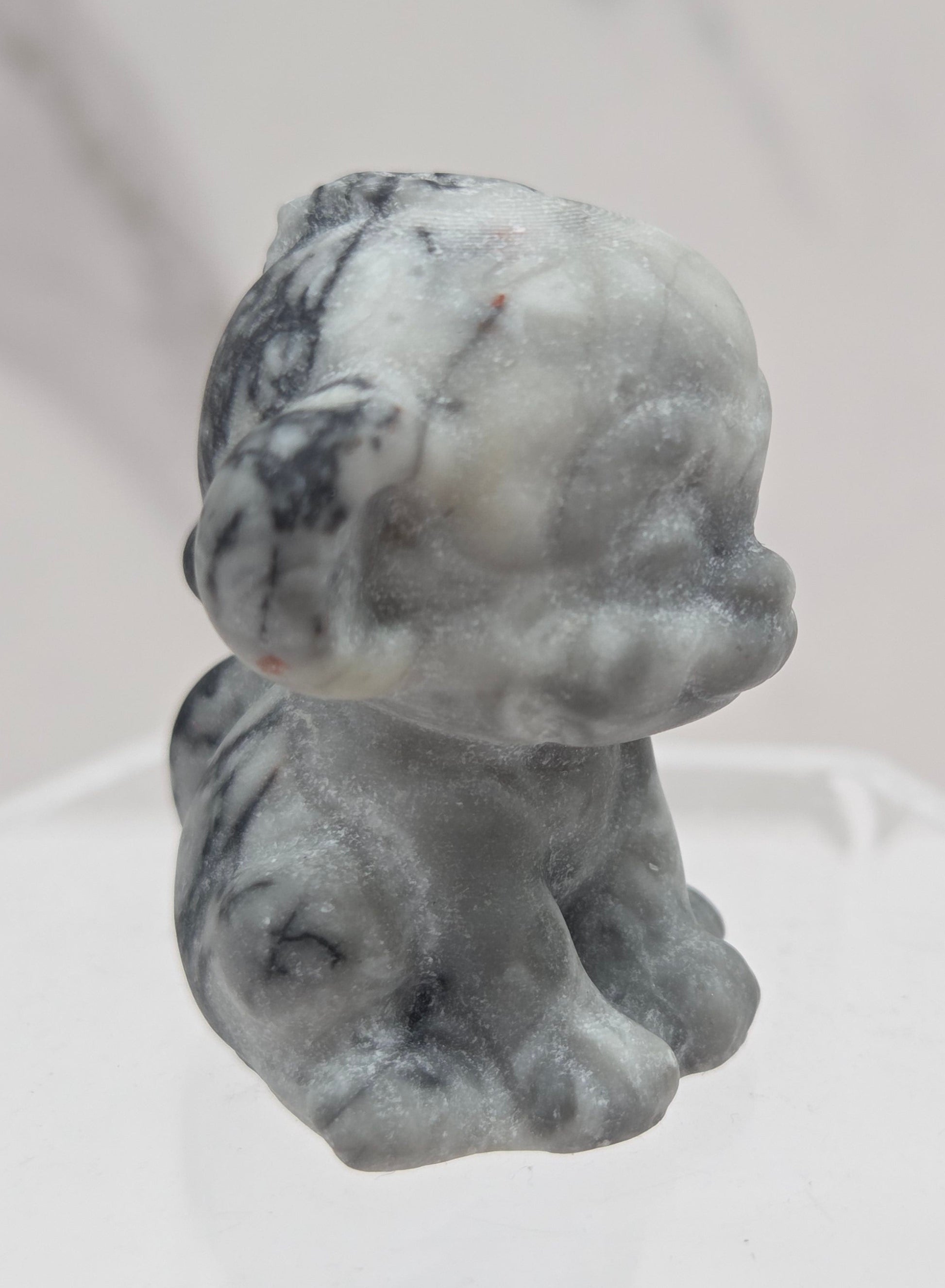 Small grey and black crystal monkey carving on a white surface