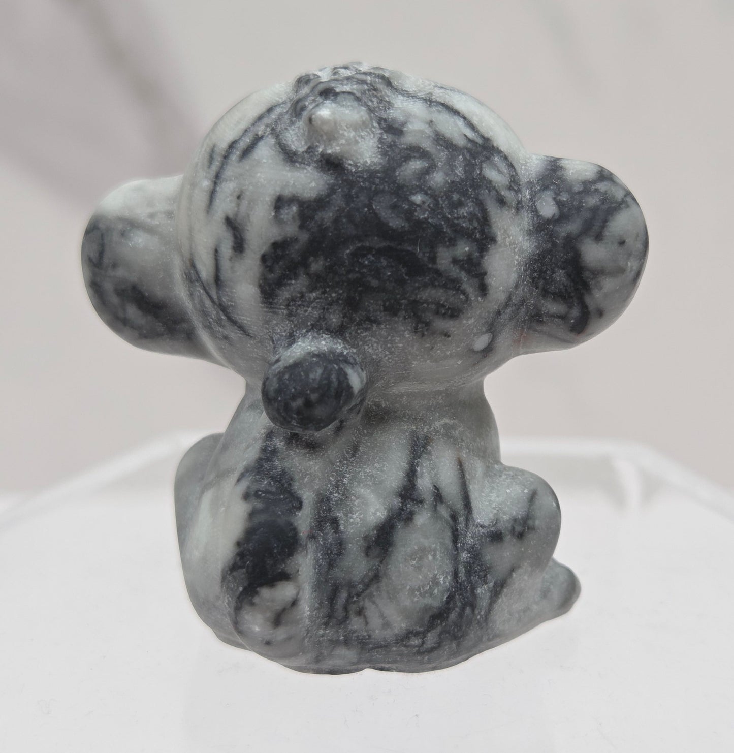 Small grey and black crystal monkey carving on a white surface