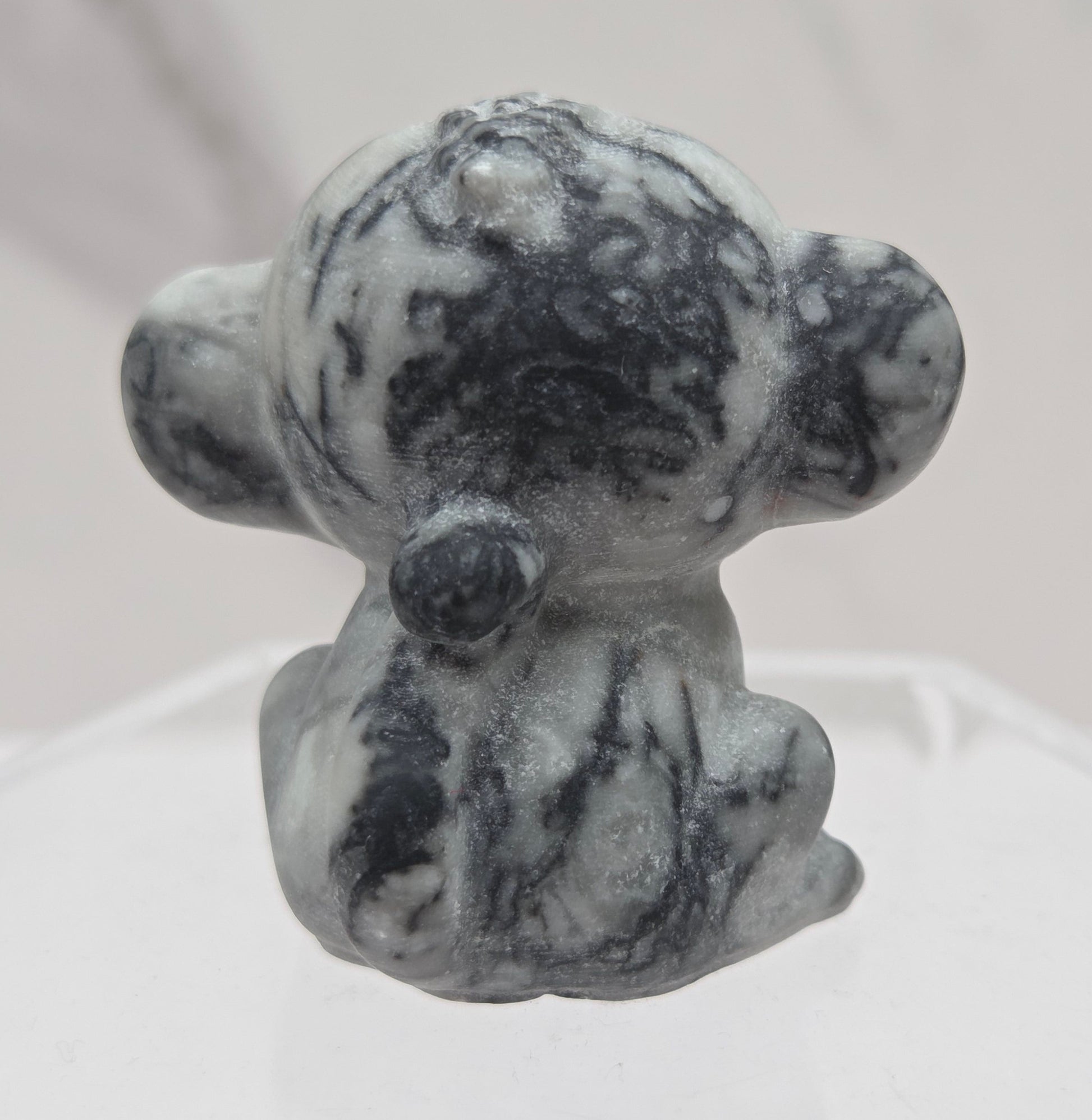 Small grey and black crystal monkey carving on a white surface