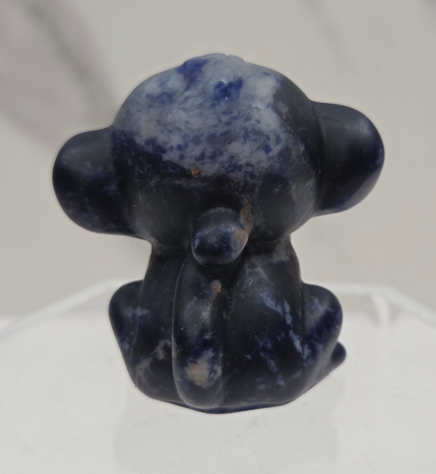 Small blue sodalite monkey carving on a white surface
