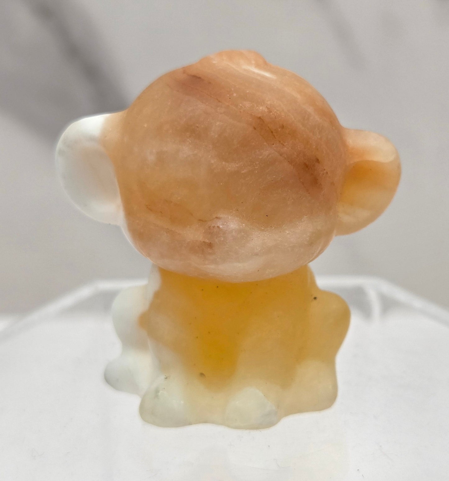 Small orange calcite monkey carving on a white surface