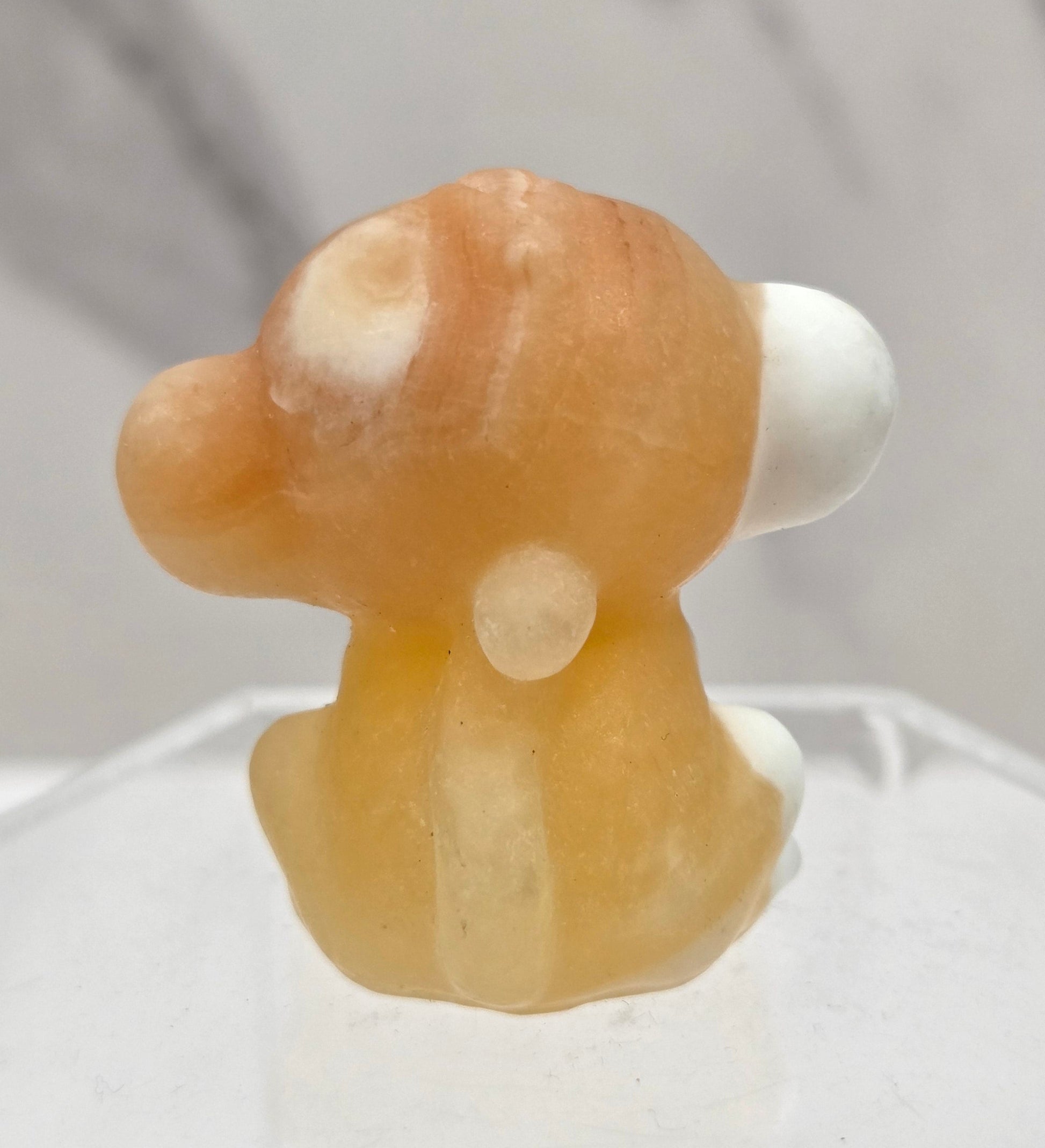 Small orange calcite monkey carving on a white surface