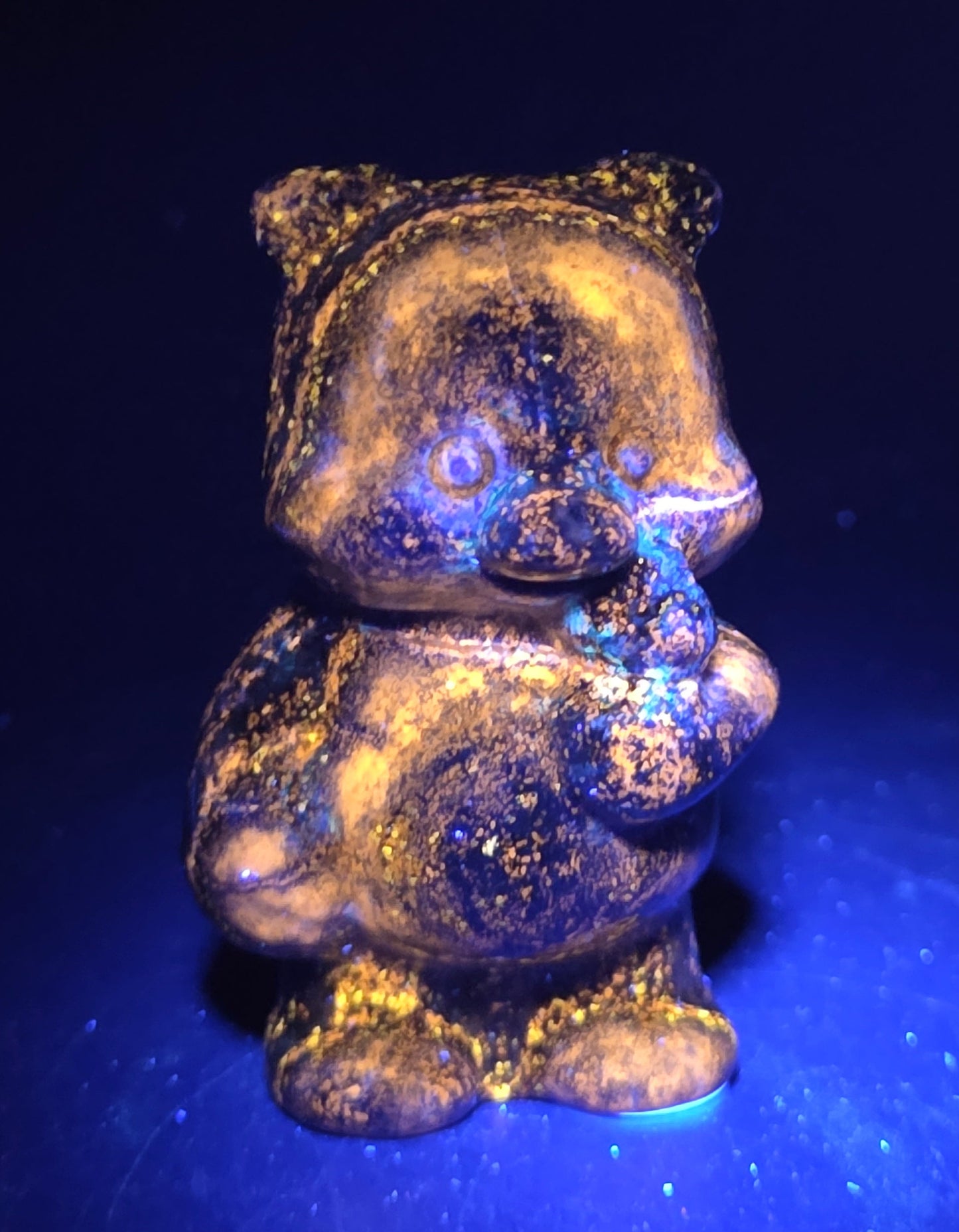 Blue Lapis carving of Pooh Bear on a black background under UV lighting