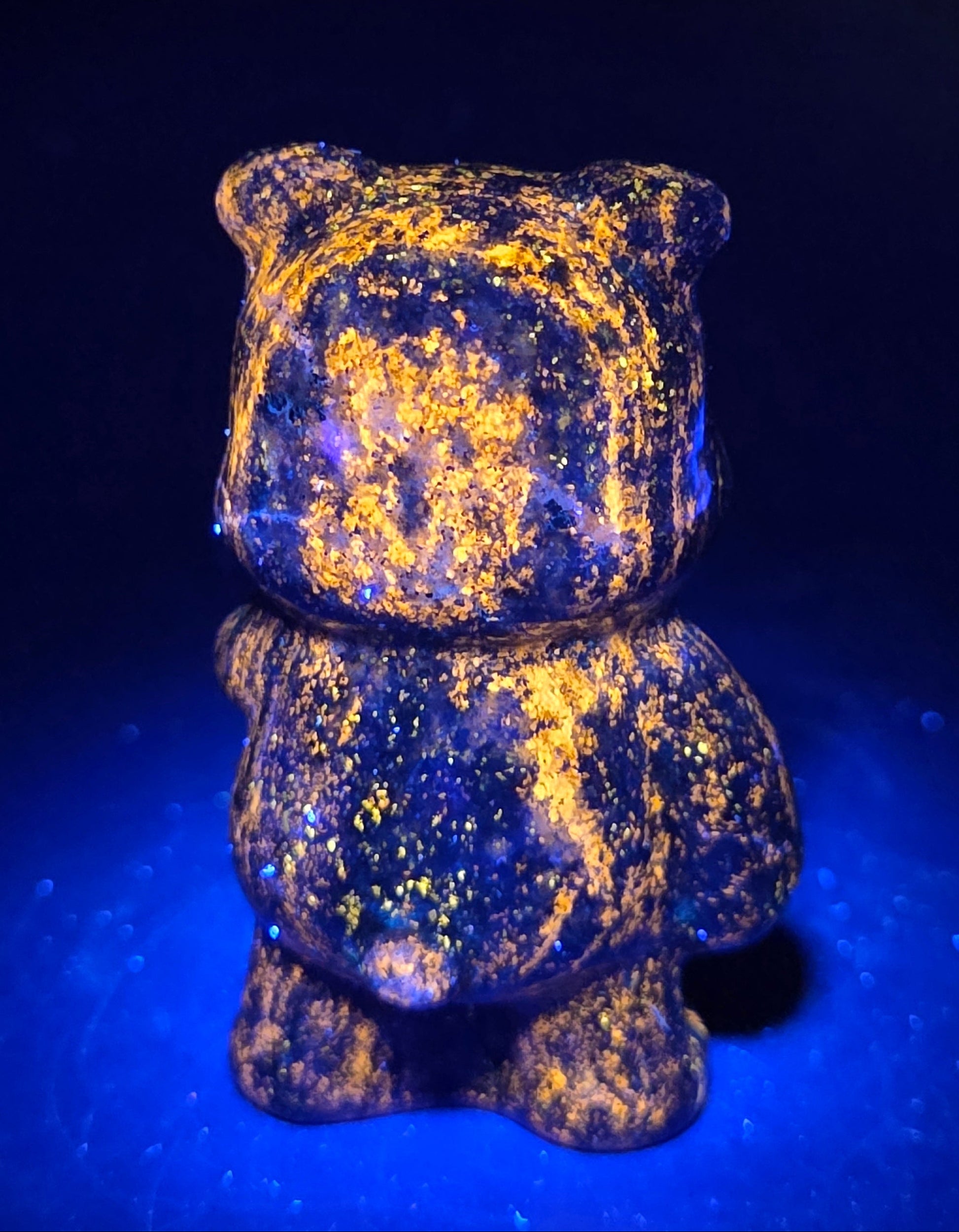 Blue Lapis carving of Pooh Bear on a black background under UV lighting