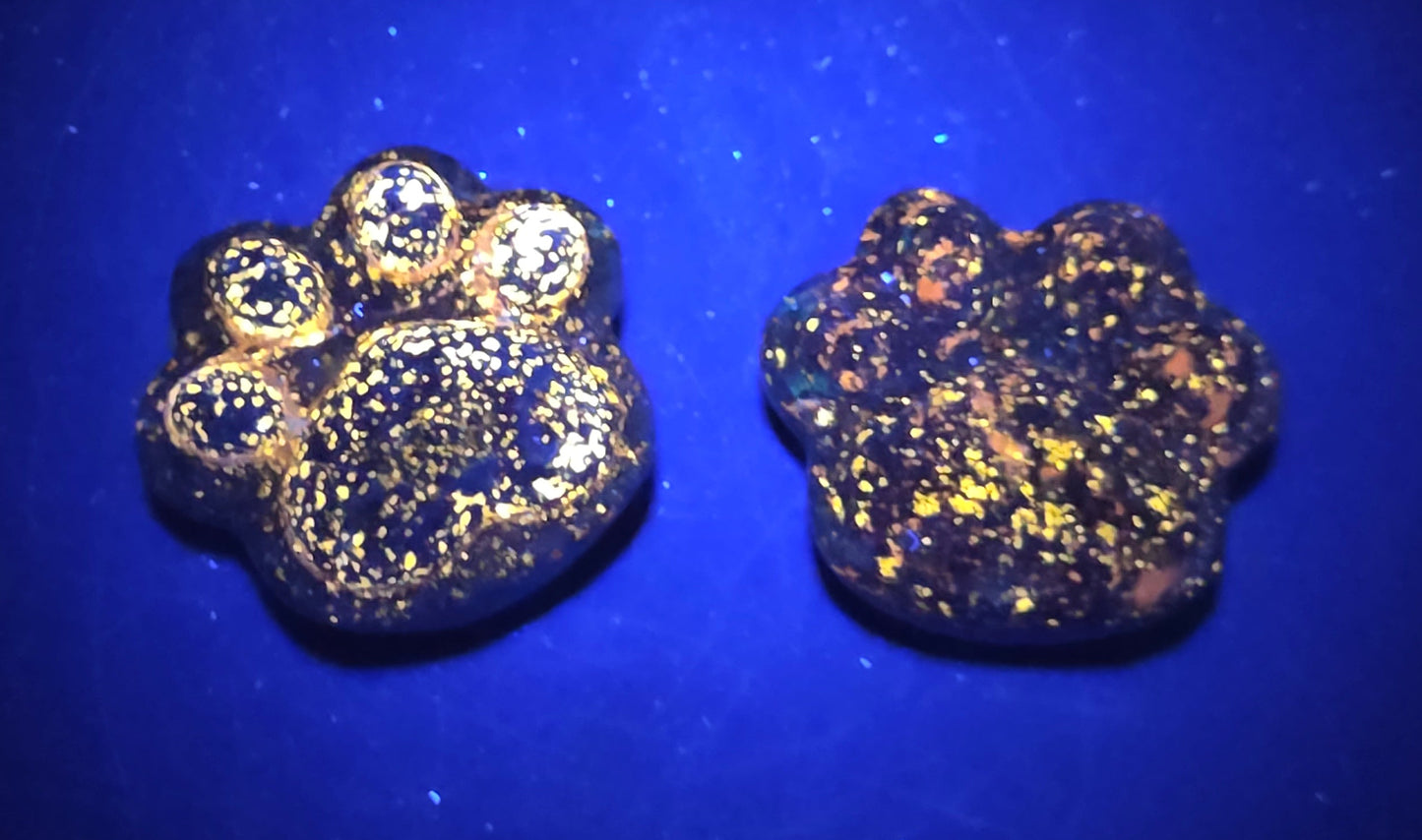 Two blue paw print-shaped objects on a black background under UV lighting