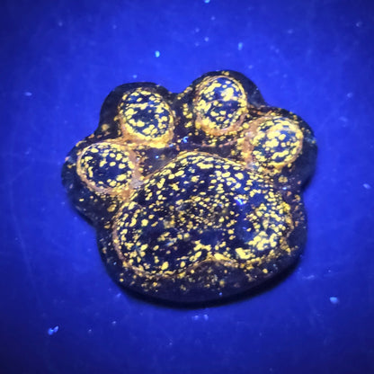 Blue lapis paw print carving on a dark background under UV lighting