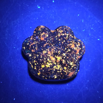 Blue lapis paw print carving on a dark background under UV lighting