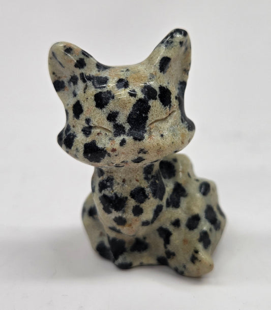 Small stone sculpture of a fox with black spots on a white background