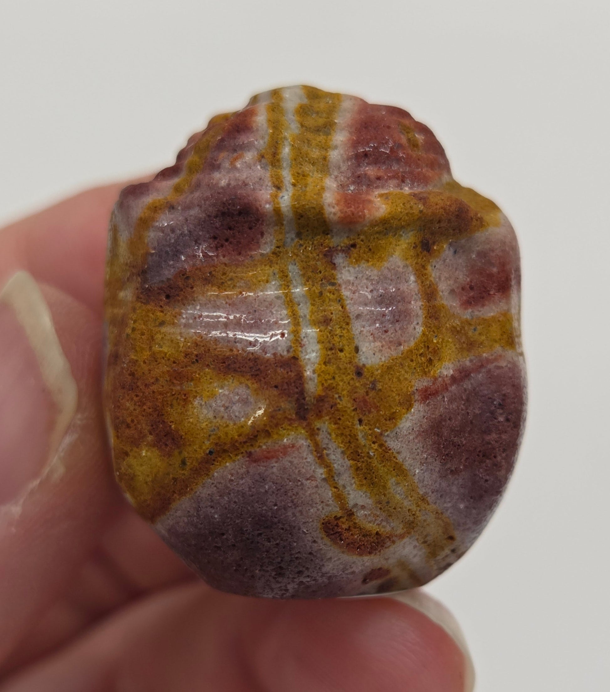 Hand holding a Mookaite rose bud carving with multiple colors against a neutral background