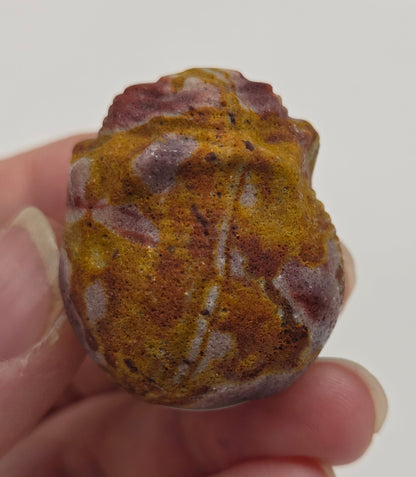 Hand holding a Mookaite rose bud carving with multiple colors against a neutral background
