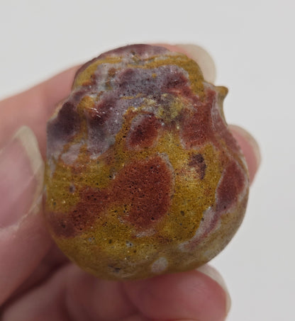 Hand holding a Mookaite rose bud carving with multiple colors against a neutral background