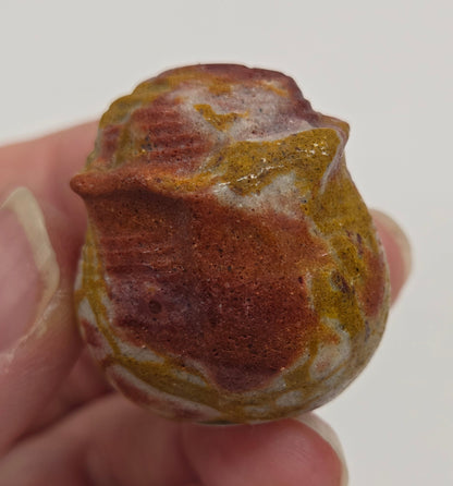 Hand holding a Mookaite rose bud carving with multiple colors against a neutral background