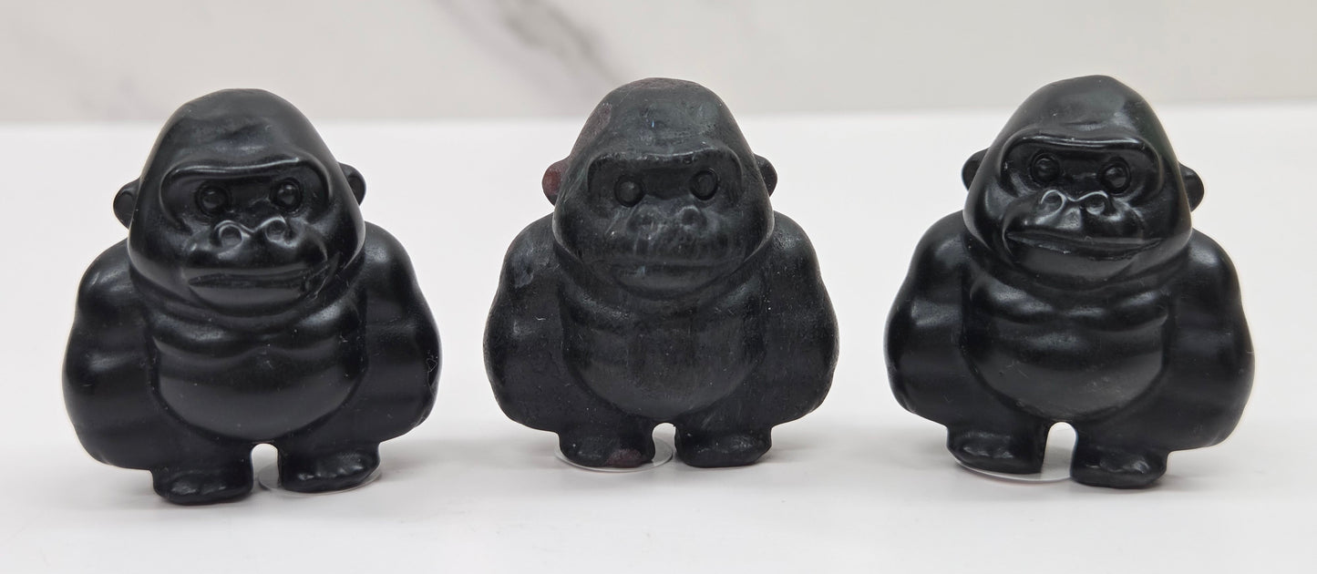 Three black gorilla figurines lined up on a white surface with a white background