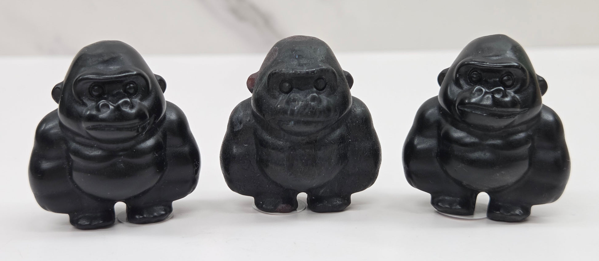 Three black gorilla figurines lined up on a white surface with a white background