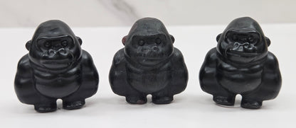 Three black gorilla figurines lined up on a white surface with a white background