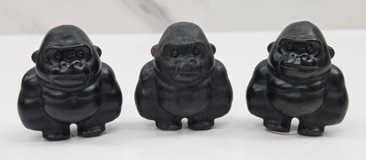 Three black gorilla figurines lined up on a white surface with a white background