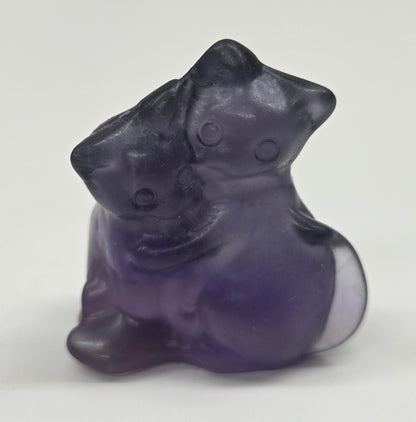 Small, purple Fluorite cat-shaped carvings  placed on a light background.