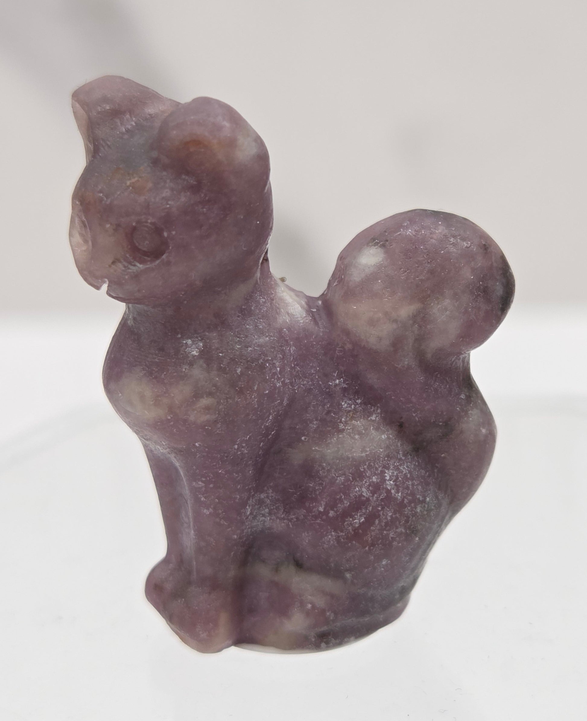 small lepidolite sculpture of a cat against a neutral background
