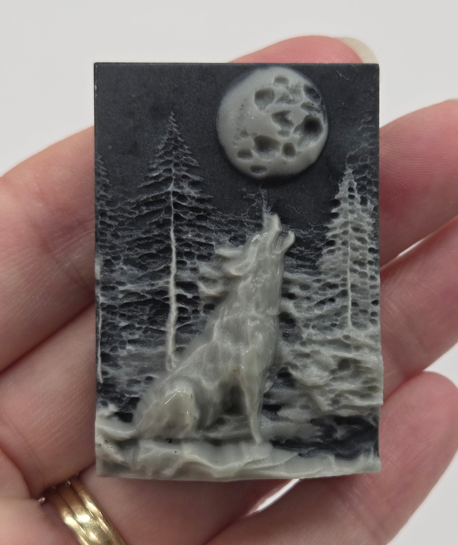 Hand holding a small rectangular Tai Chi carving with a design of a wolf and moon on a gray background.