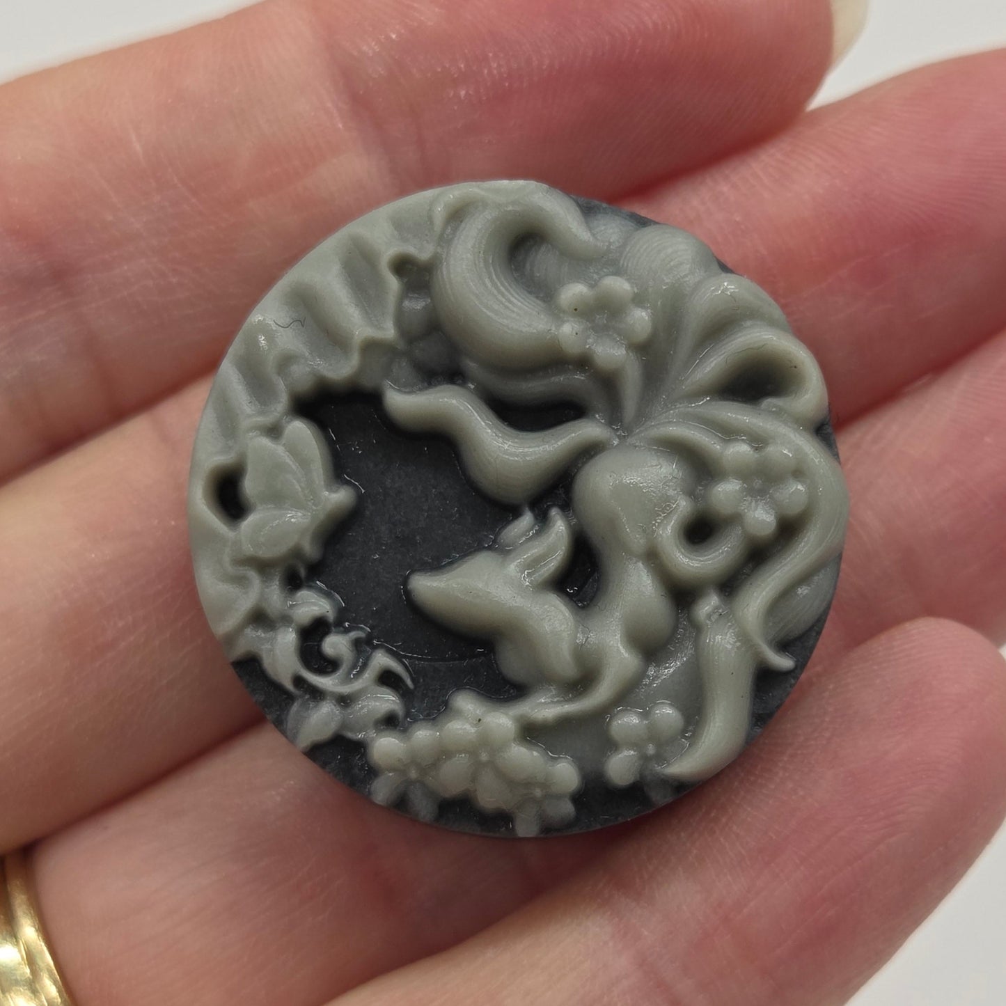 Hand holding a small rectangular Tai Chi carving with a design of a 9 tail fox on a gray background.