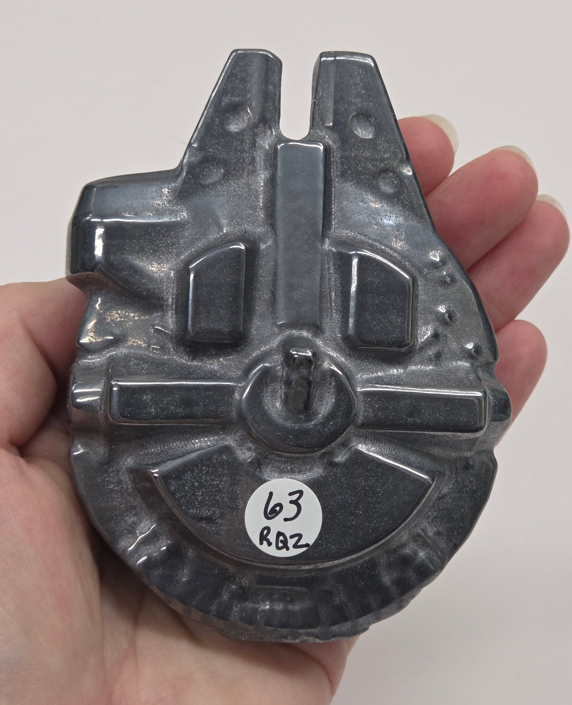 Hand holding a metallic looking Millennium Falcon carving on a white background