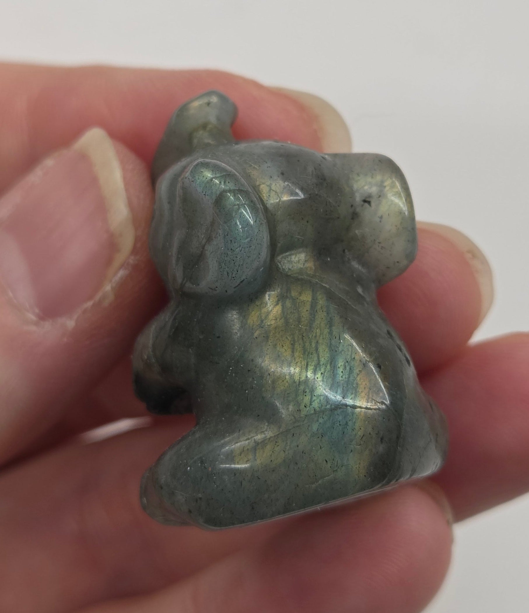 Hand holding a small Labradorite sculpture of an elephant against a white background