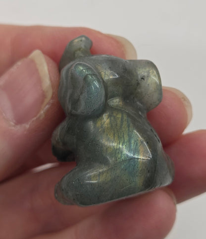 Hand holding a small Labradorite sculpture of an elephant against a white background