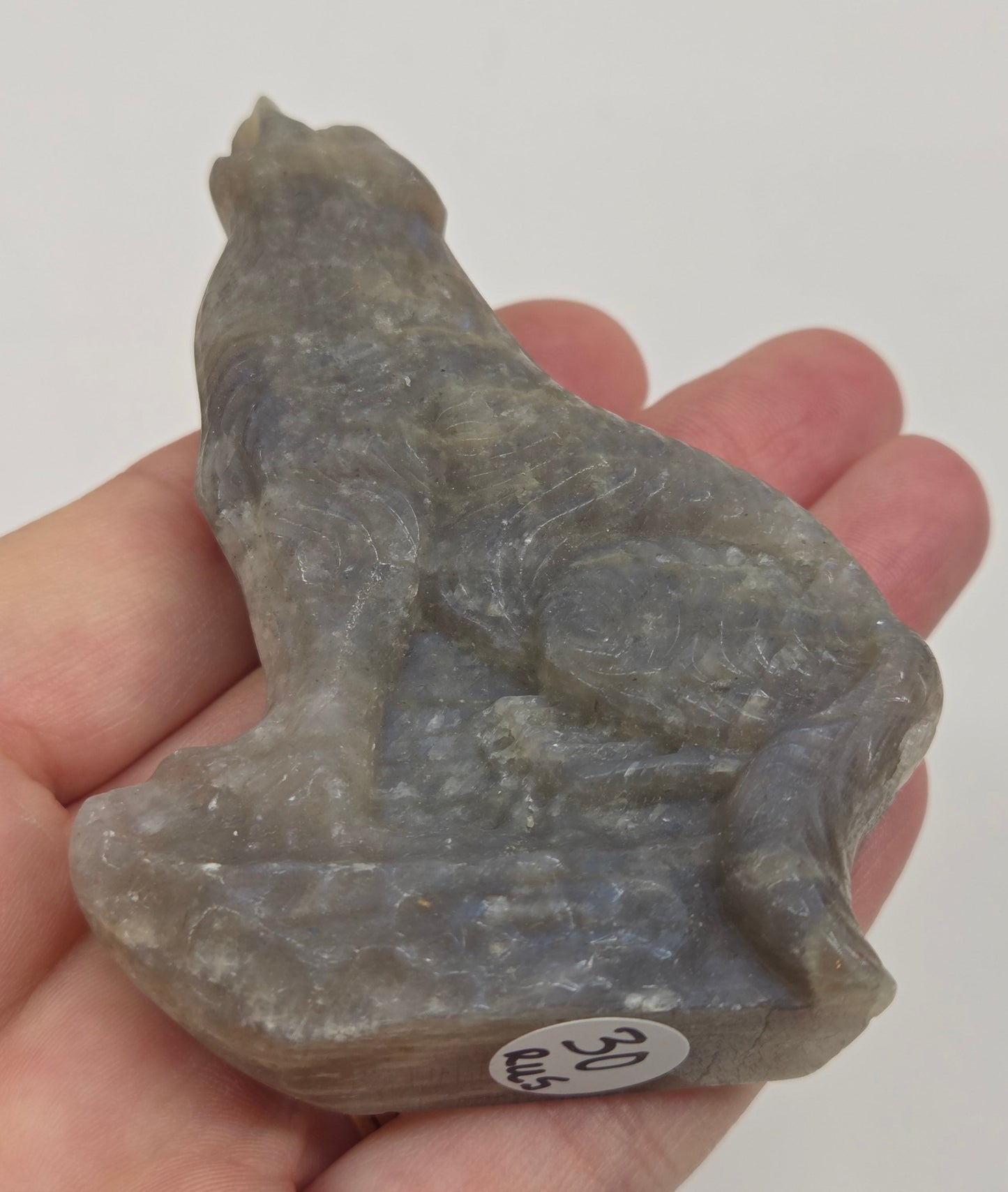 Hand holding a small Moonstone sculpture of a wolf on a plain background