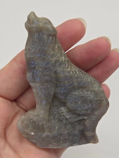 Hand holding a small Moonstone sculpture of a wolf on a plain background