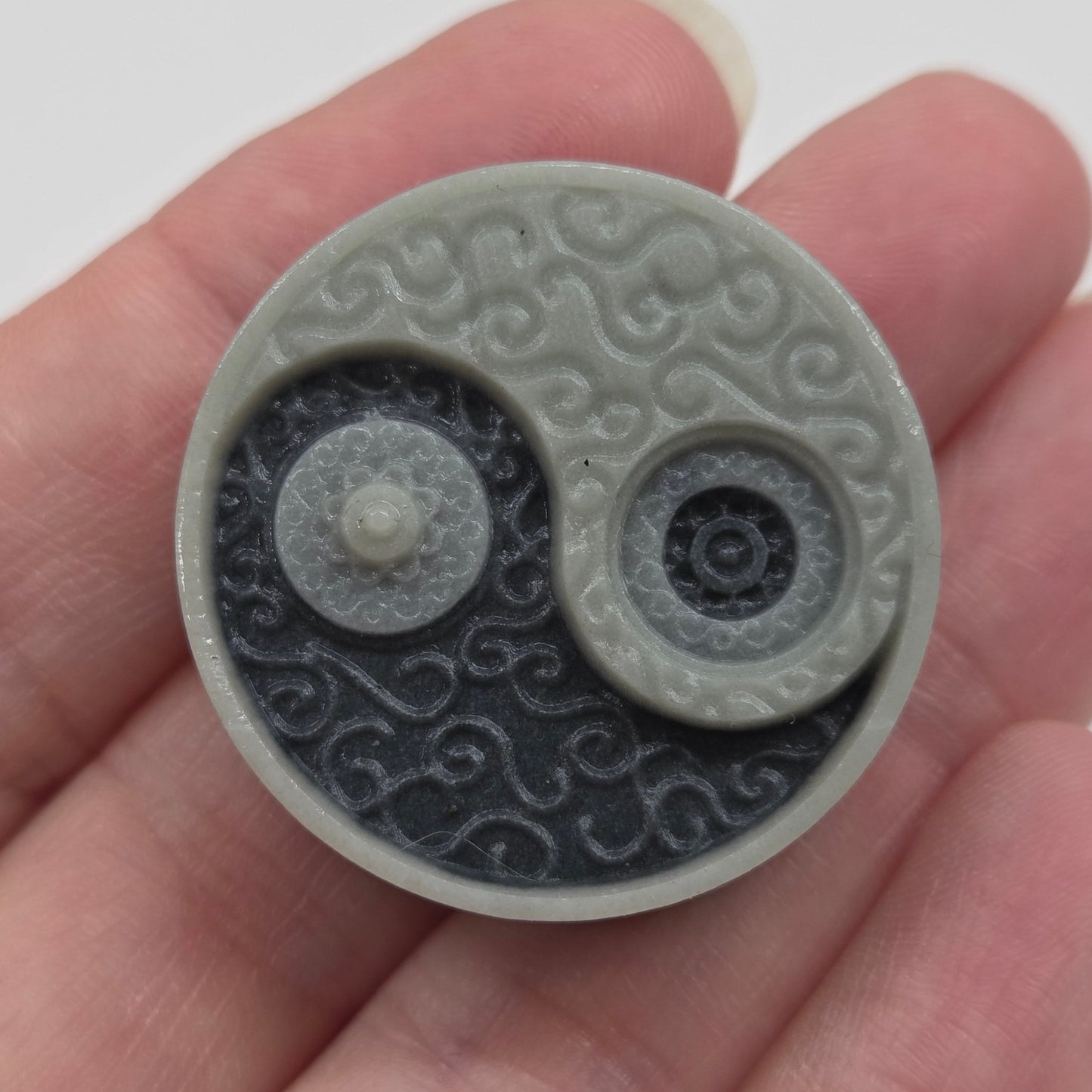 Hand holding a small rectangular Tai Chi carving with a yin yang design 