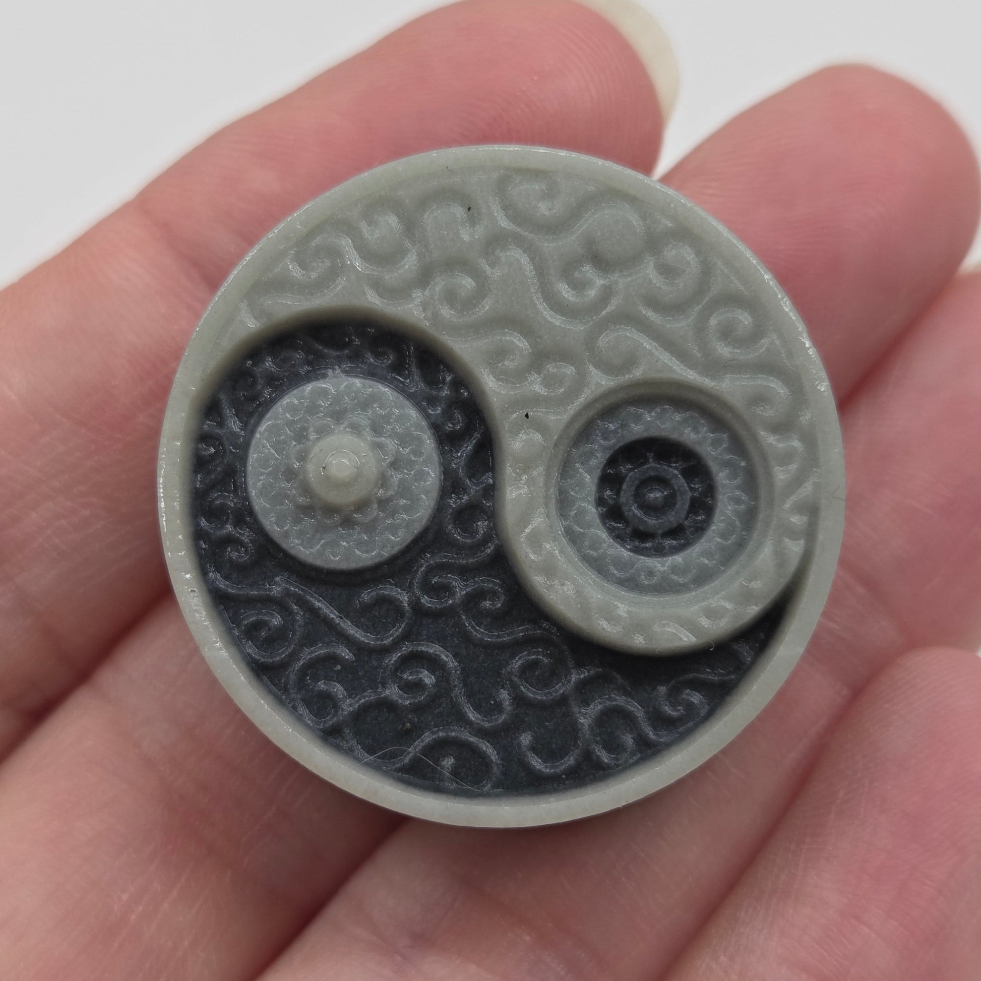 Hand holding a small rectangular Tai Chi carving with a yin yang design 