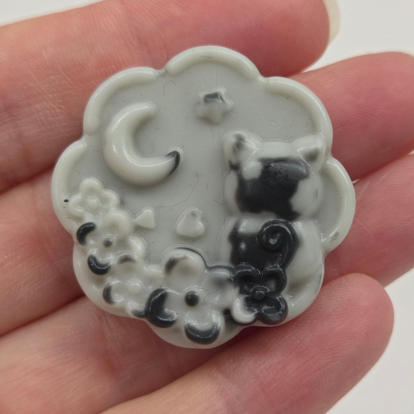 Tai Chi small cloud-shaped object with black cat designs held in a hand against a white background