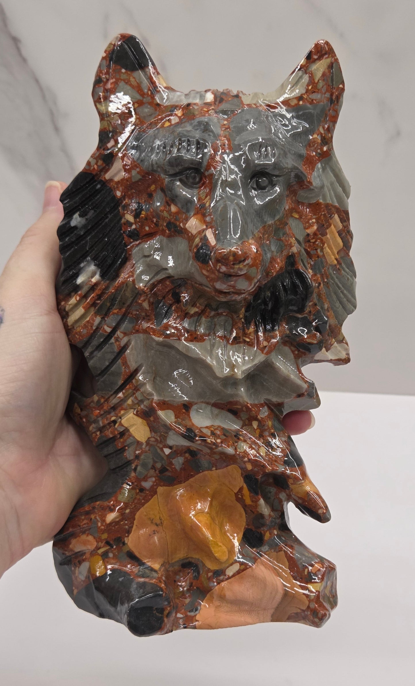 Hand holding a wolf carving with a mix of brown, gray, and black colors on a white background
