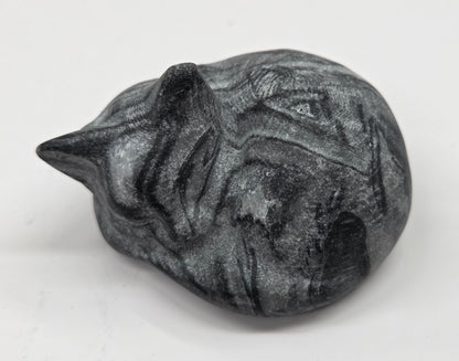 Fossil Shell Jasper sleeping cat carving with black and grey coloring on a white background
