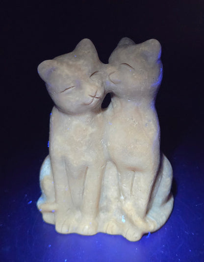 Brown amber calcite carving of a cat couple on a white background under UV light