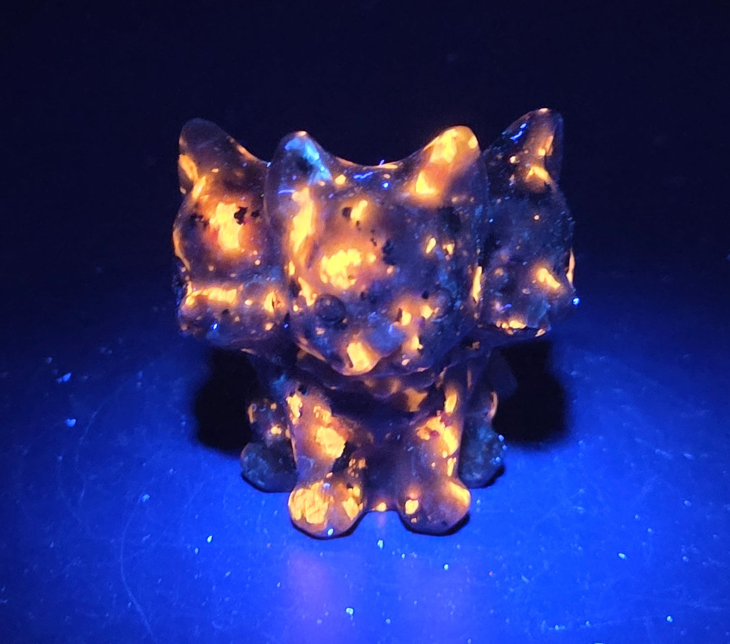 Yooperlite small crystal mythological cerberus animal figurines on a white surface under UV lighting
