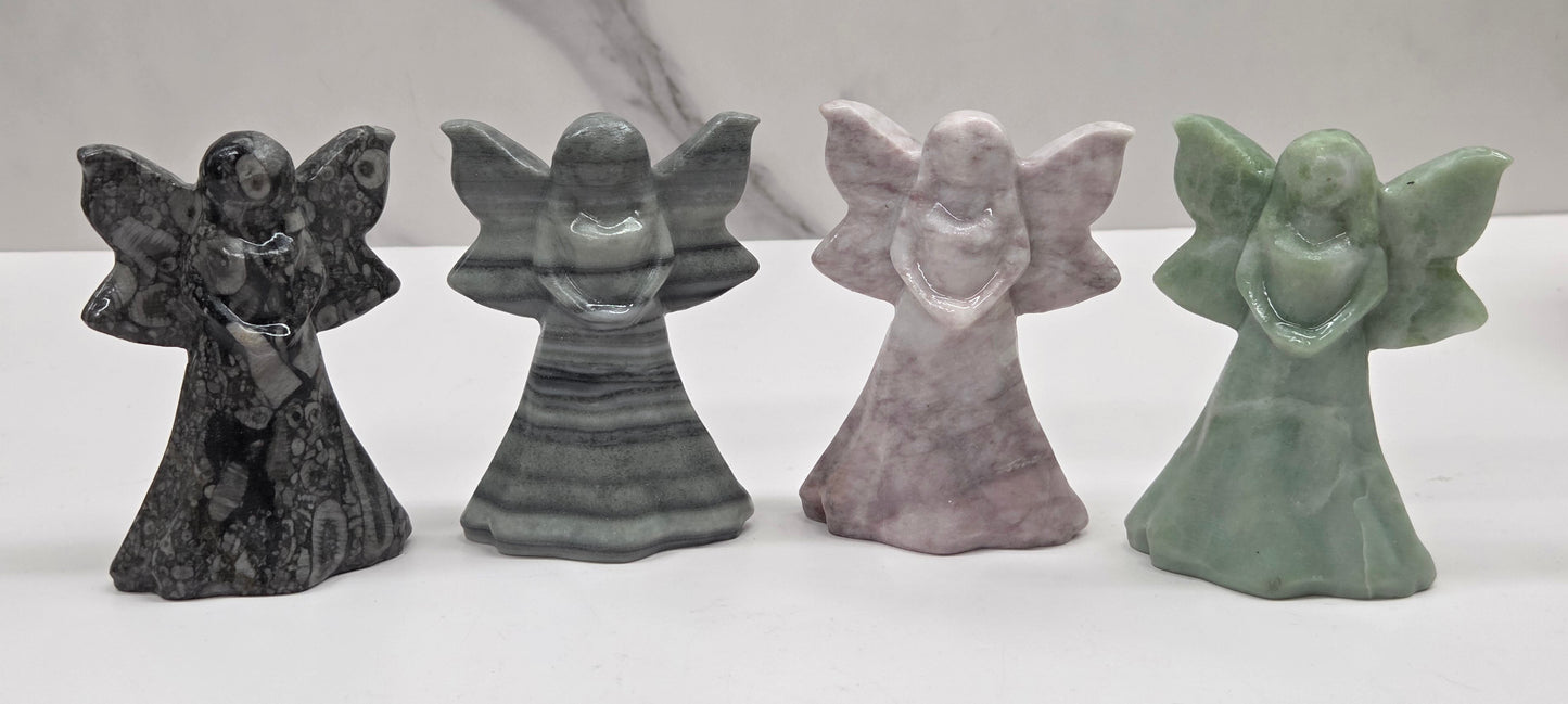 Four stone fairy figurines in different colors on a white surface with a marble background.