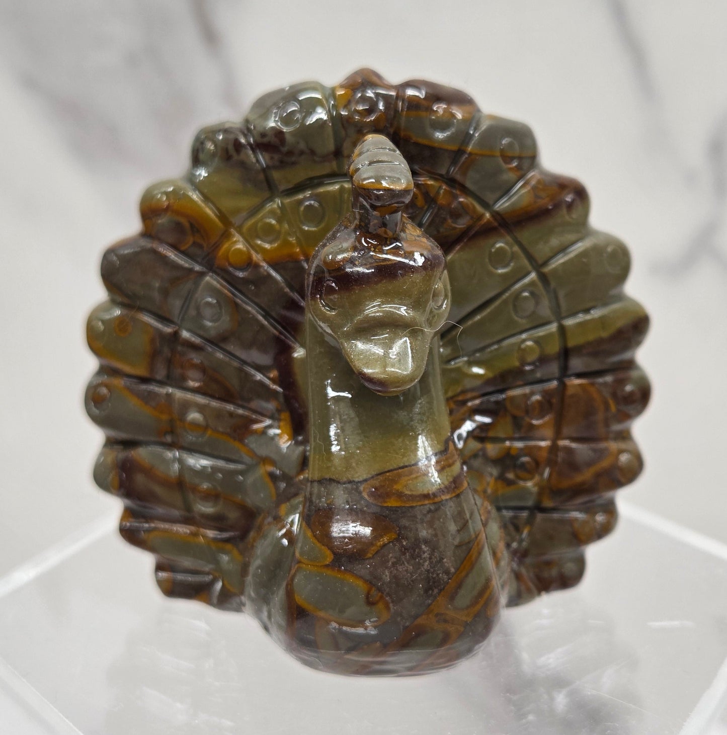 Decorative bamboo jasper peacock carving on a clear stand against a white background