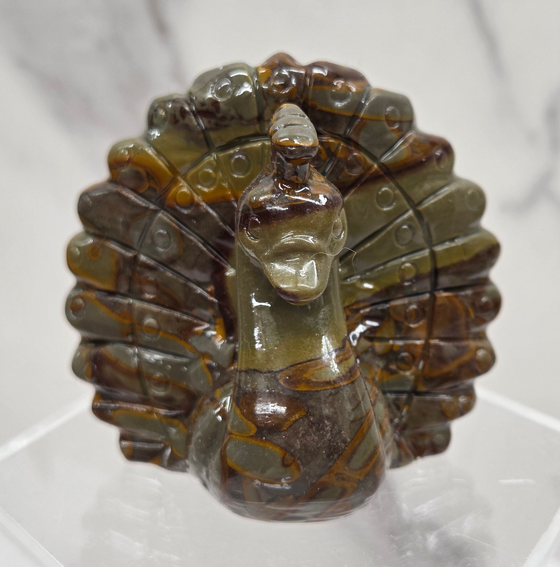 Decorative bamboo jasper peacock carving on a clear stand against a white background