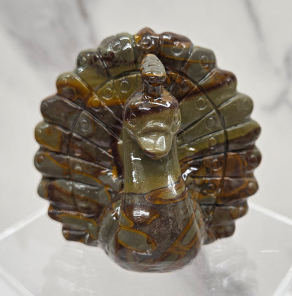 Decorative bamboo jasper peacock carving on a clear stand against a white background