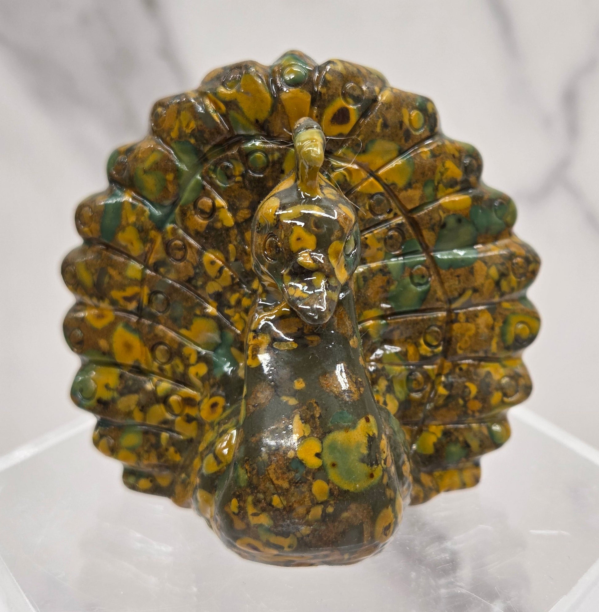 Decorative ajooba jasper peacock carving on a clear stand against a white background