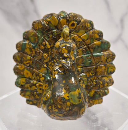 Decorative ajooba jasper peacock carving on a clear stand against a white background