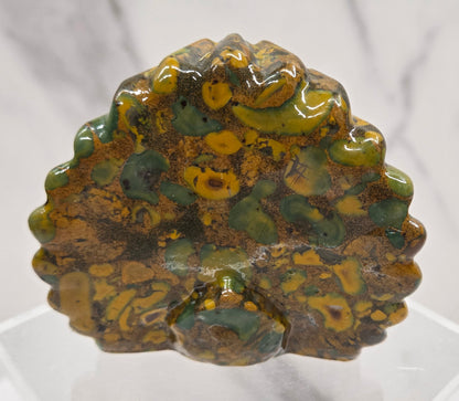 Decorative ajooba jasper peacock carving on a clear stand against a white background
