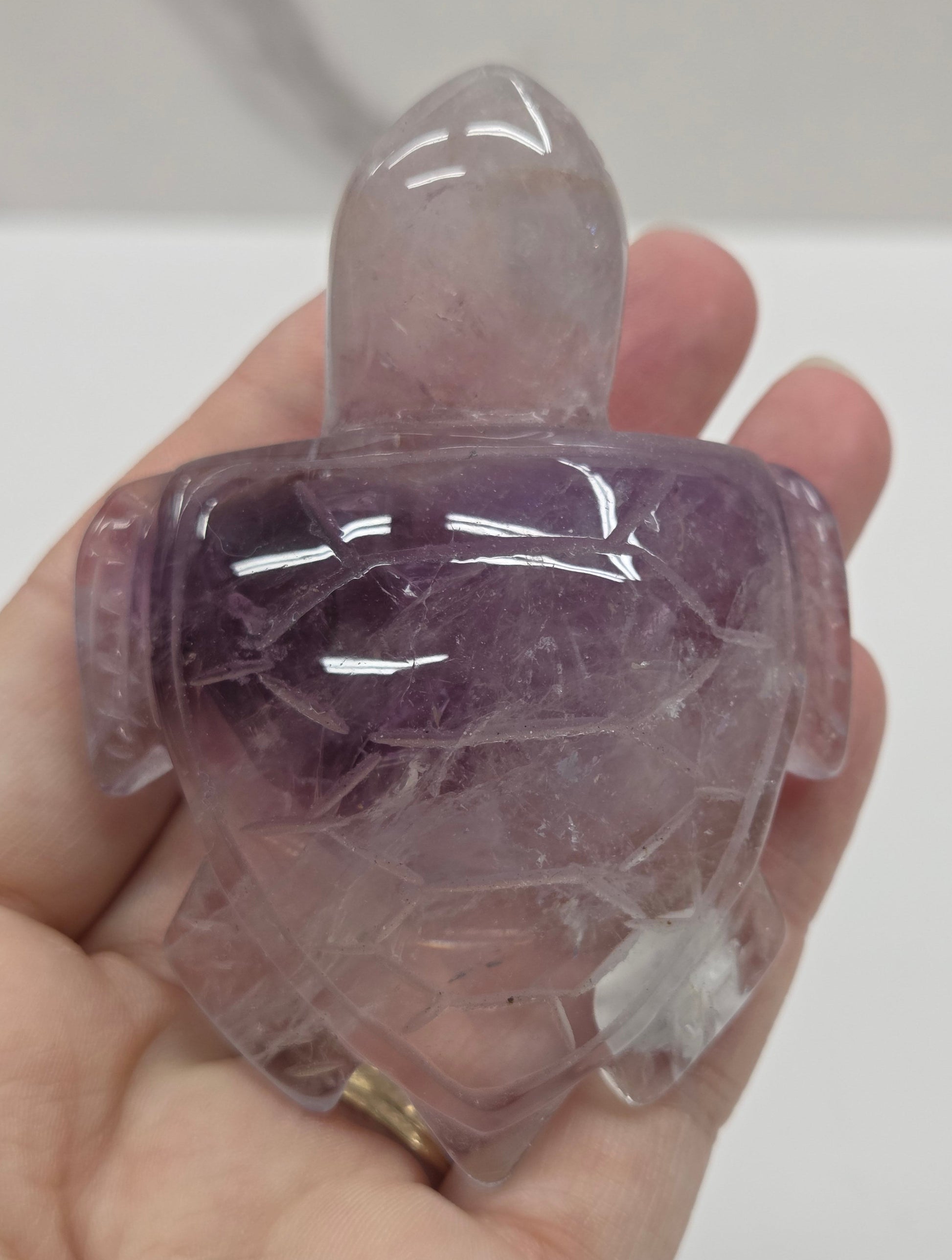 Hand holding a phantom amethyst sea turtle carving on a white background