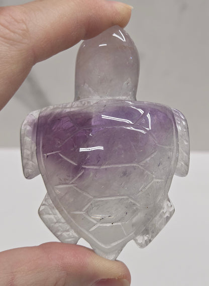 Hand holding a phantom amethyst sea turtle carving on a white background