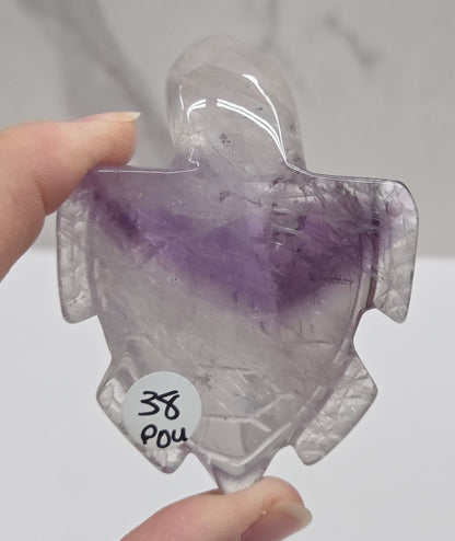 Hand holding a phantom amethyst sea turtle carving on a white background