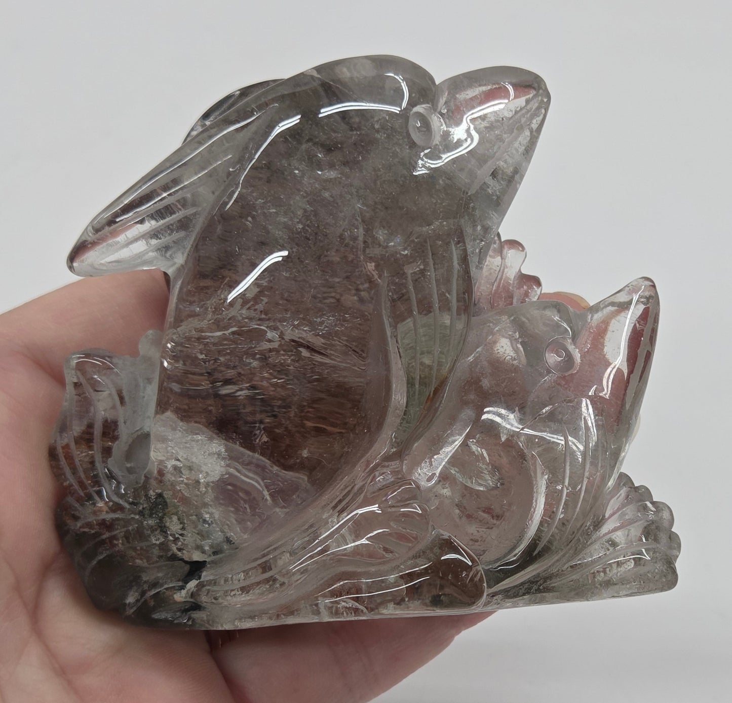 Hand holding a dolphin in a wave shaped garden quartz crystal carving on a white background