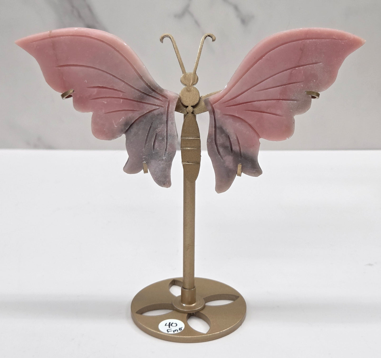 Pink Opal crystal wing carvings on a gold metal stand on a white background