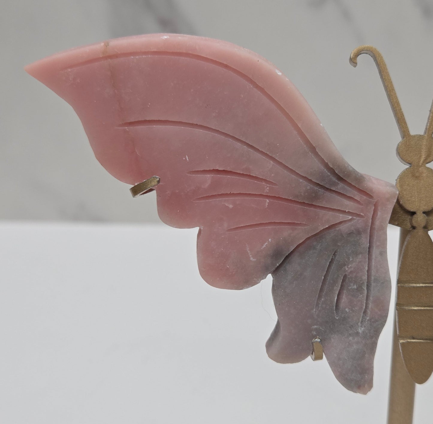 Pink Opal crystal wing carvings on a gold metal stand on a white background