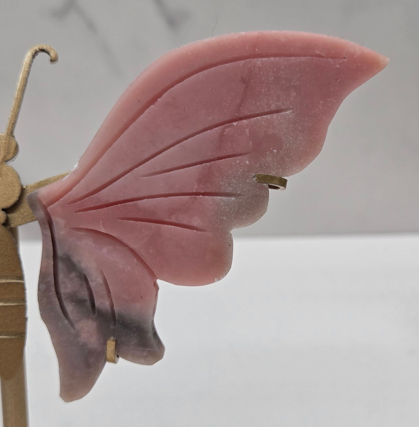 Pink Opal crystal wing carvings on a gold metal stand on a white background